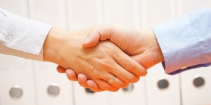 business man and woman are handshaking over documents in with office in background